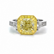 A yellow diamond ring with a square-shaped center stone and a halo, set in a silver-colored band with small clear accent diamonds, shown on a white background.